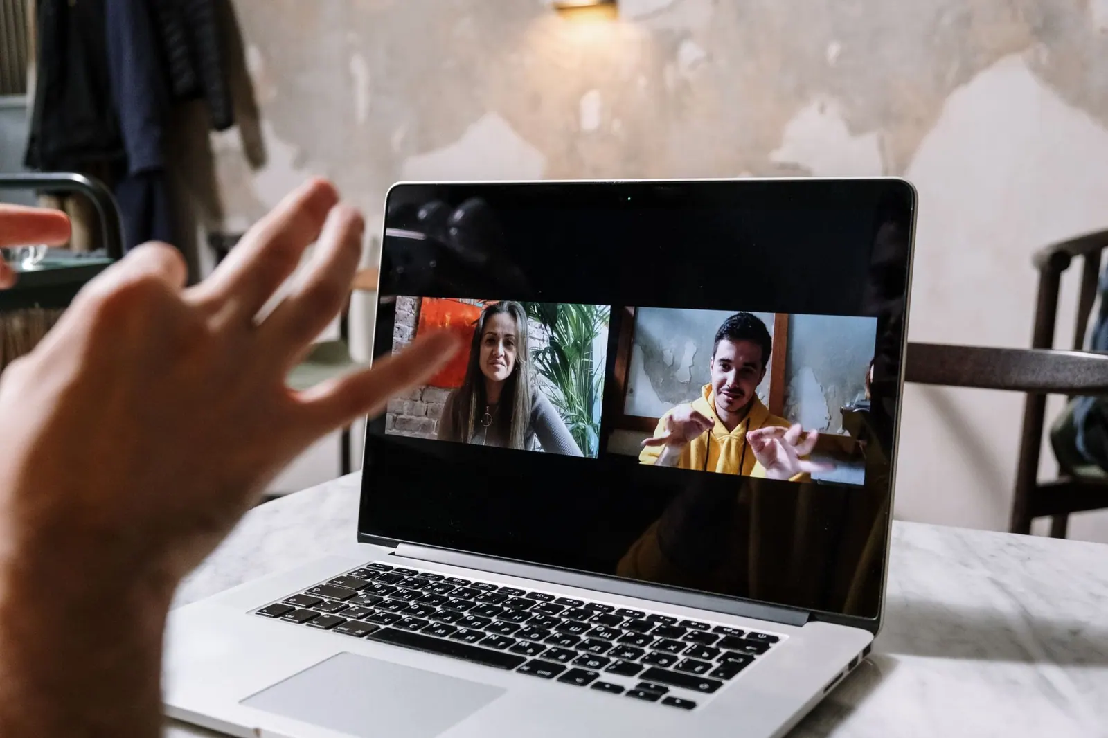 Hands gesturing during a video call on a laptop screen, showing two people in a virtual meeting. Team collaboration alternatives explained with examples